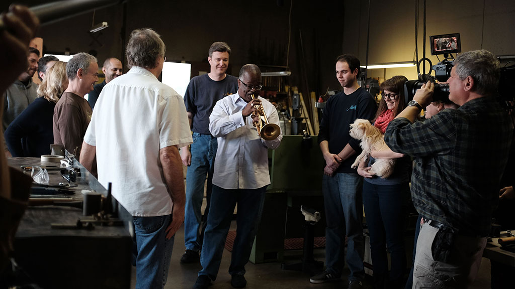 Monette employees and Craft in America crew listen as Scotty Barnhart tests the latest trumpet