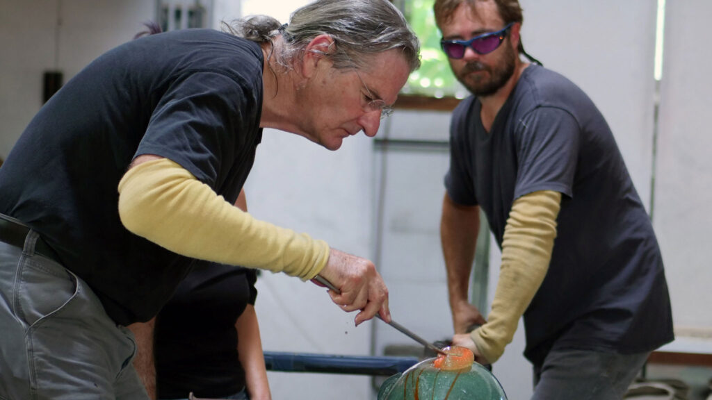 Glass artist Richard Jolley shapes glass with lead assistant James A. Breed. Denise Kang photo. HARMONY episode of Craft in America