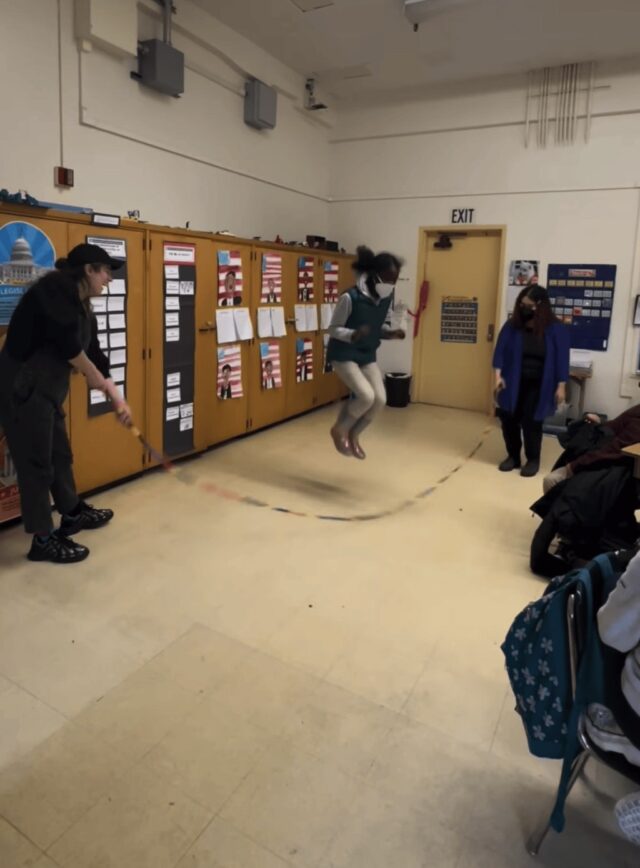 Artist Calder Kamin, Sam from Craft in America, and 4th graders enjoy a game of jump rope with a marker-cap toy they created together