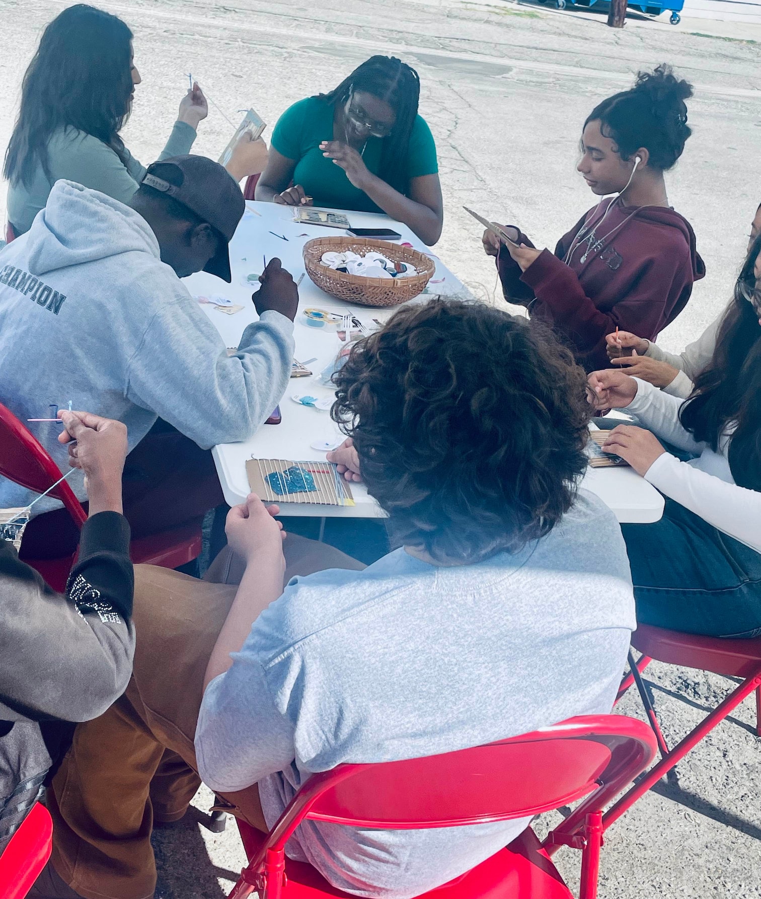 a few high school students are deep in thought, chatting with each other as they sit and weave their collage and yarn designs together