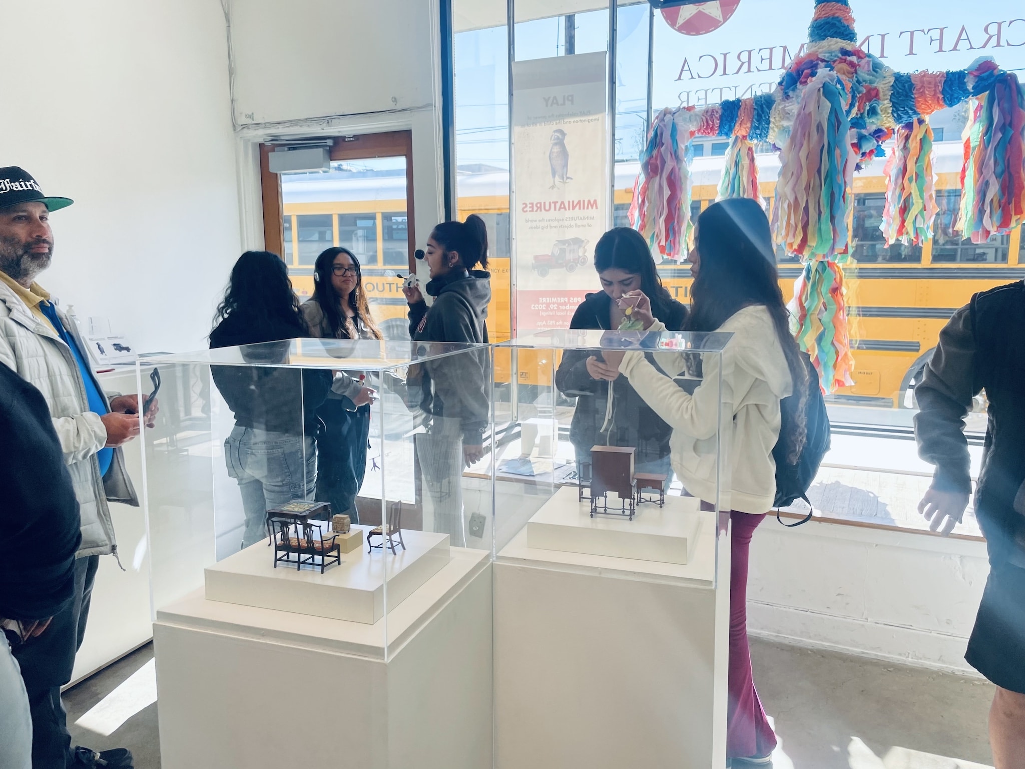 Candid moment of Fairfax High School art students studying Mark Murphy's displayed miniatures and Loren Robletto's giant window Piñata
