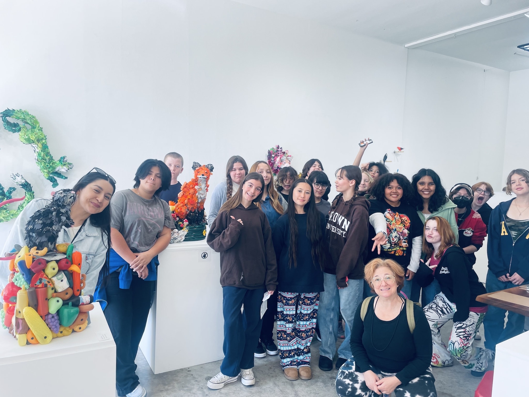 Smiling group photo of 2 dozen or so enthustiastic Paul Revere M.S. art class with their teacher among the many colorful plastic/found object sculptures of Calder Kamin