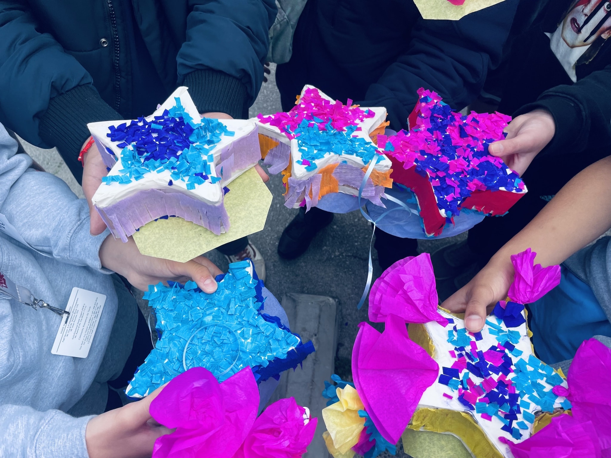 close up photo of colorful star pinata's with varying shades of blues purples and oranges held in a group by Van Nuys High School student hands reaching from off-camera