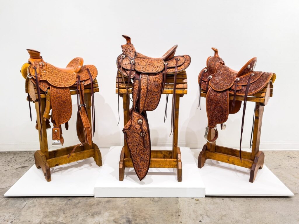 Three engraved leather saddles displayed on wooden saddle stands