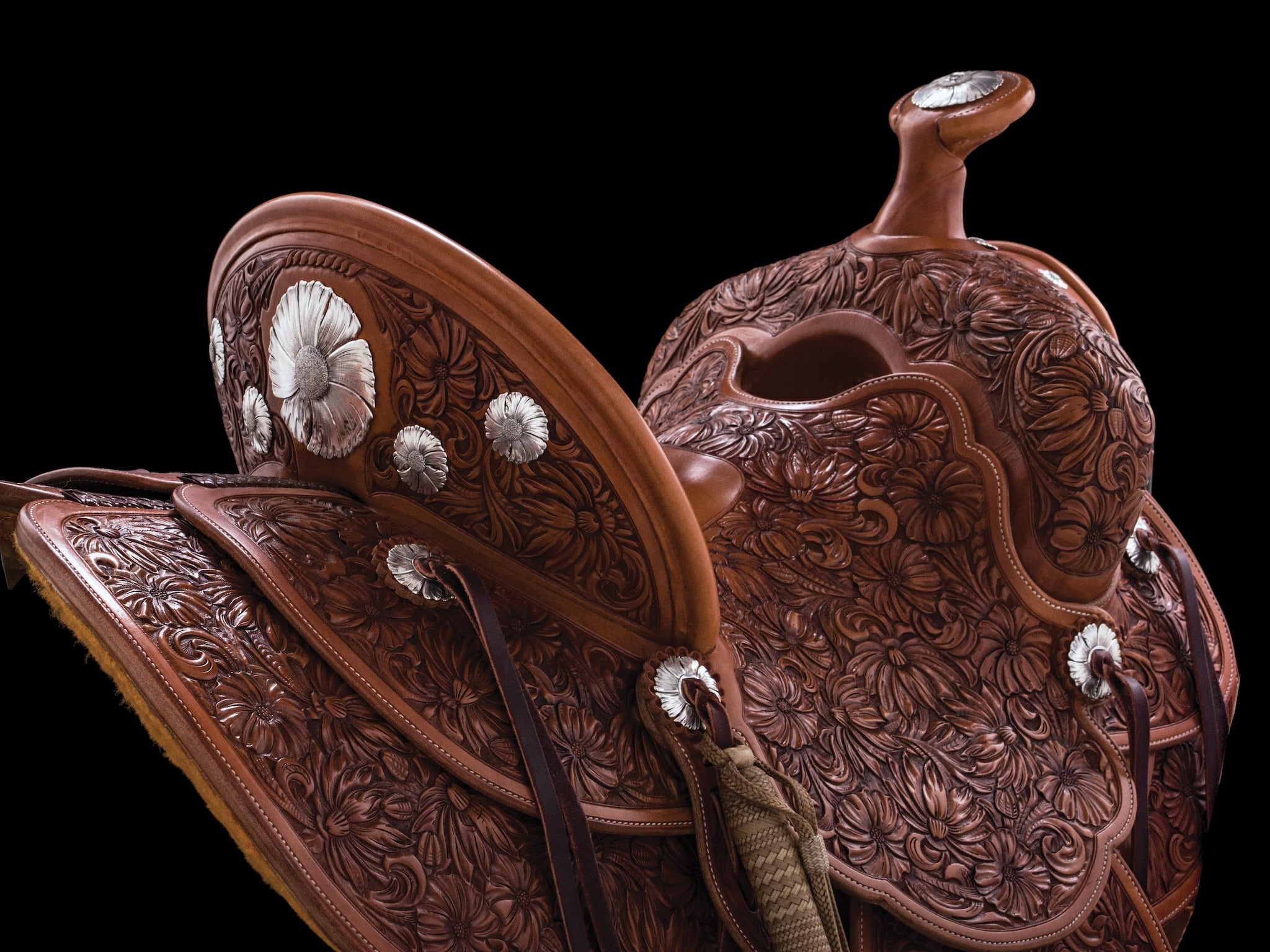 Close up up hand-engraved floral patterns and silver hardware on a brown leather saddle