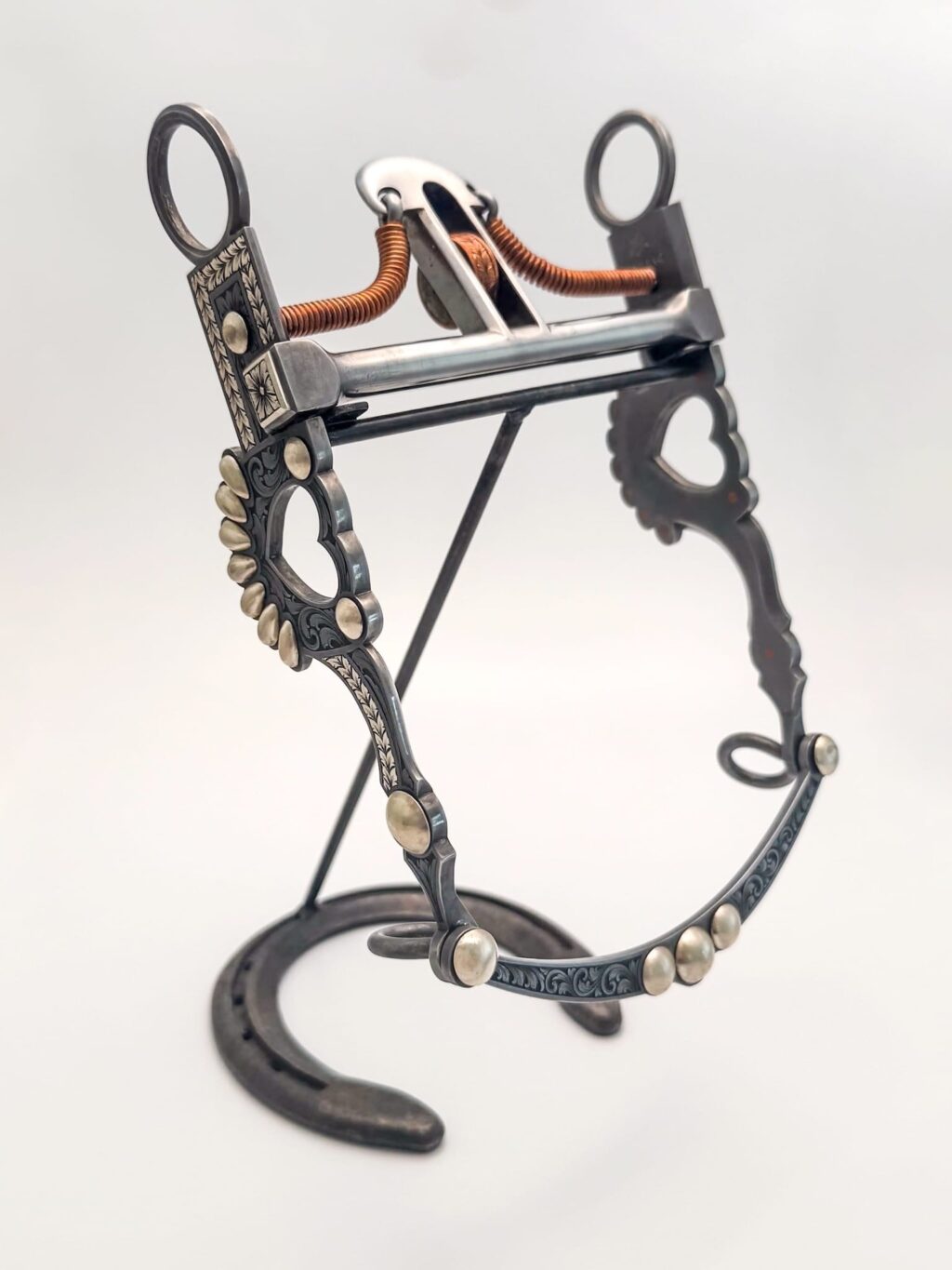 Ornate bit made of inlayed sterling silver with relief engraving, displayed on a stand